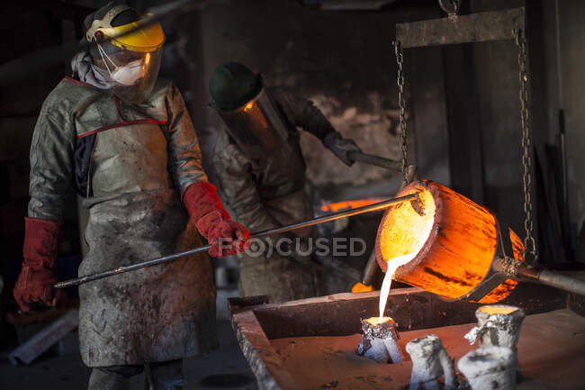 Металлурги, работающие в литейном производстве, разливают расплавленную бронзу — стоковое фото