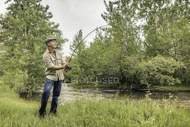 Junger Mann mit Schiebermütze am Ufer des Flusses angeln — Stockfoto