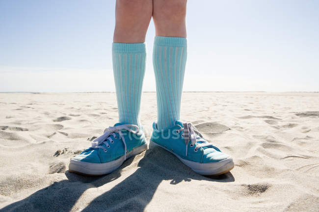 Дитина стоїть на пляжі в шкарпетках і кросівках — стокове фото