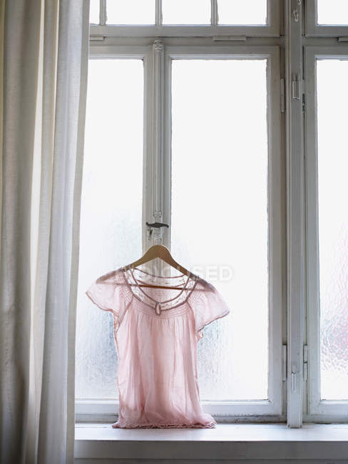 Pink blouse hanging on window handle — Stock Photo