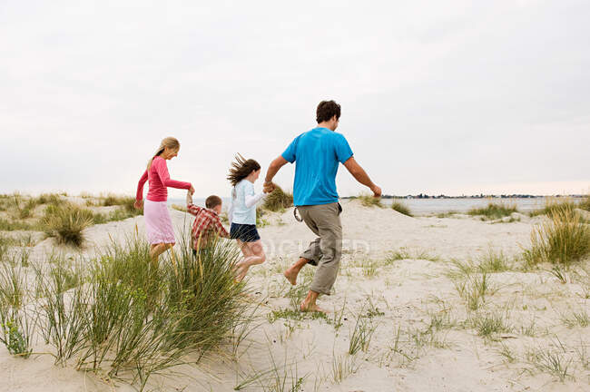 Joven familia corriendo en la playa - foto de stock