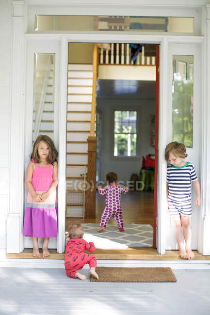 Niño y niña viendo a un niño arrastrándose por la puerta de la casa - foto de stock