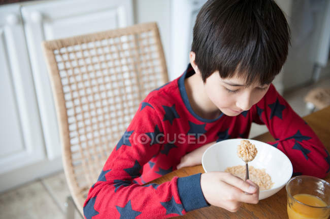 Niño comiendo cereales de desayuno en la mesa - foto de stock