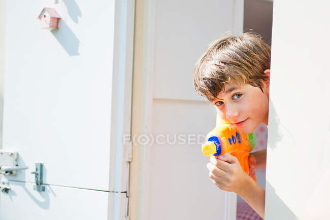 Boy holding water pistol and peering out of caravan, portrait — Stock Photo