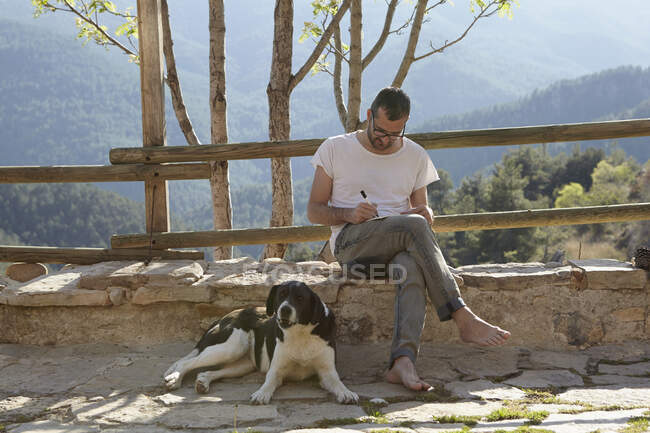Середній дорослий чоловік з собакою пише нотатки на патіо — стокове фото