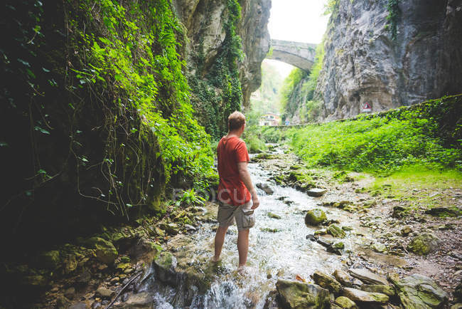 Homme debout dans ruisseau, collines rocheuses et pont en pierre en arrière-plan, Garda, Italie — Photo de stock