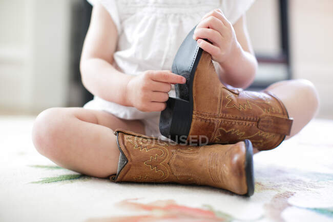 Neck down view of female toddler sitting on floor wearing cowboy boots — Stock Photo
