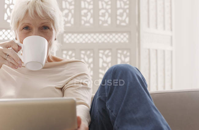 Femme âgée buvant du café et travaillant sur ordinateur portable — Photo de stock