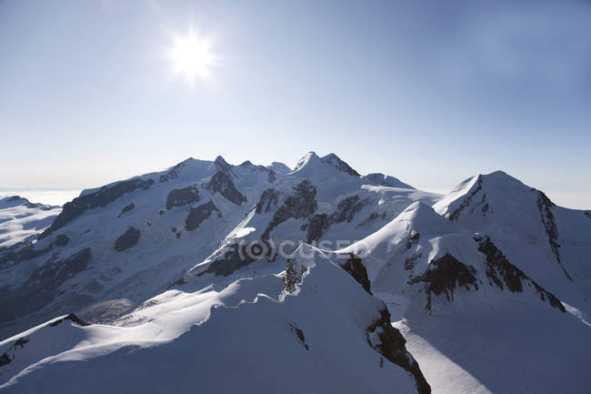 Snowcapped rocky mountains with shining sun — Stock Photo