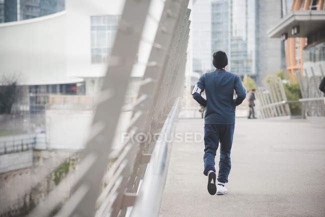 Rear view of young male runner on city footbridge — Stock Photo