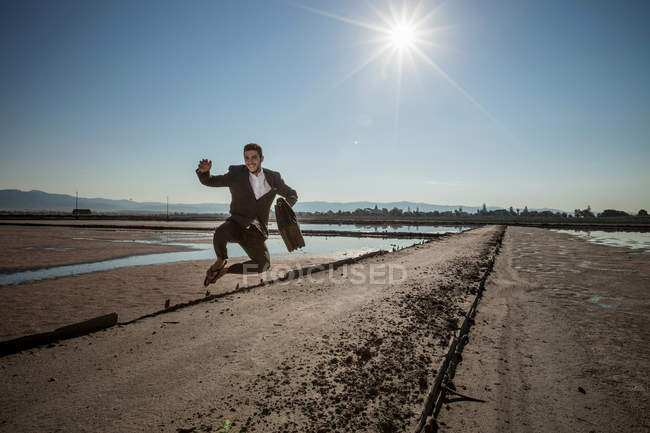 Mid adult businessman carrying briefcase jumping mid air at beach — Stock Photo