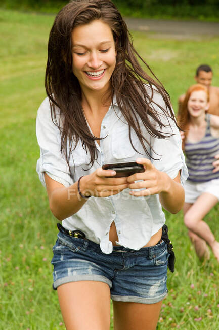 Девочка-подросток смотрит на мобильный телефон во время прогулки по сельской местности с друзьями — стоковое фото