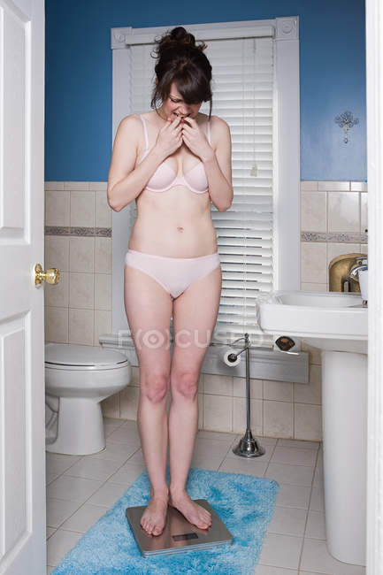 Junge Frau wiegt sich auf Badezimmerwaage — Stockfoto