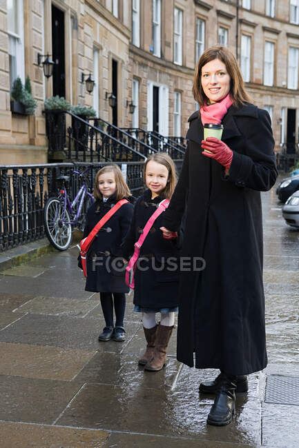 Madre y dos hijas de pie en el pavimento - foto de stock