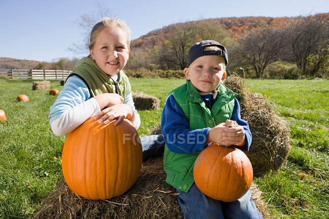 Niño y niña en el campo con calabazas - foto de stock