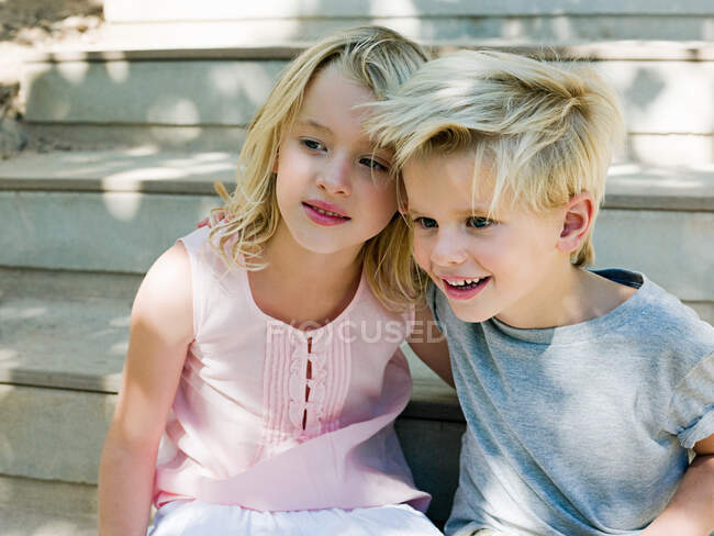 Hermano y hermana sentados en escalones de madera - foto de stock