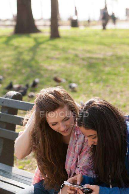 Jovens mulheres compartilhando música no parque — Fotografia de Stock