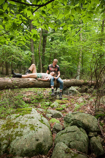 Pareja relajándose juntos en el registro en el bosque - foto de stock