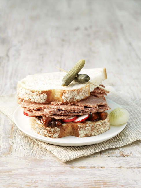 Carne en conserva, encurtidos y sándwich de rábano en rodajas de pan blanco con pepinillos y cebollas en escabeche - foto de stock