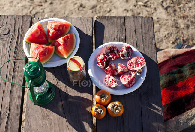 Нарізані фрукти на тарілках на столі для пікніка на сонячному світлі — стокове фото