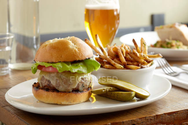 Vista frontal de hamburguesa y papas fritas en la mesa del restaurante con cerveza - foto de stock