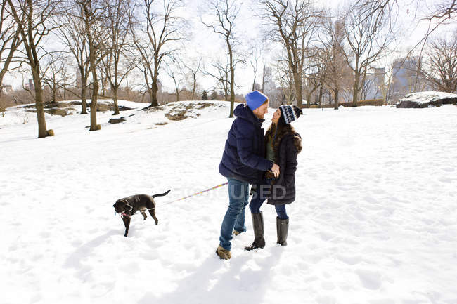 Romantic young couple standing together in snow with dog, Central Park, New York, USA — Stock Photo