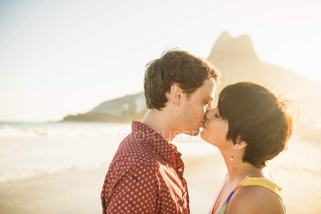 Junges paar küsst sich am sonnenuntergang, strand von ipanema, rio, brasilien — Stockfoto