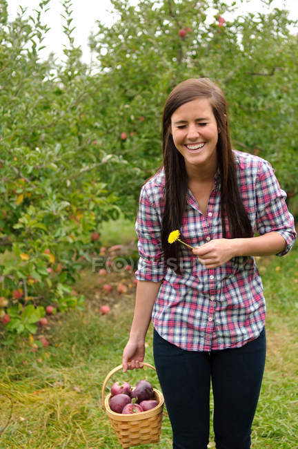 Young woman in orchard, laughing and holding a flower — Stock Photo