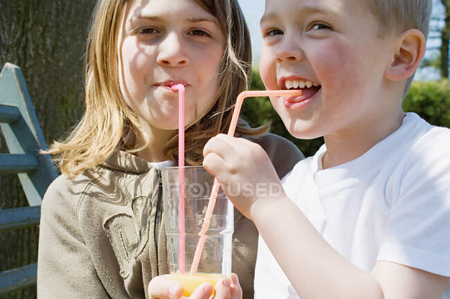 Niño y niña compartiendo bebida - foto de stock