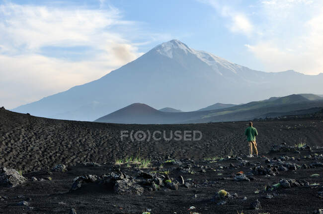 Homem em pé no campo de lava com o Vulcão Tolbachik no fundo, Península de Kamchatka, Rússia — Fotografia de Stock