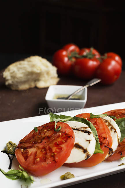 Sliced vine tomatoes and mozzarella with basil and dressing — Stock Photo