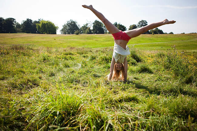 Молодая женщина делает стойку на руках в поле — стоковое фото