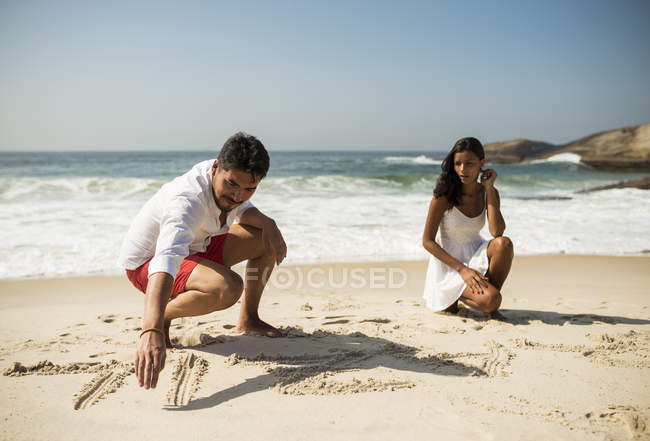 Pareja escribiendo en arena en la playa de Arpoador, Rio De Janeiro, Brasil - foto de stock