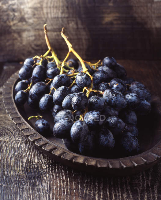 Unch of black grapes in vintage wooden bowl — Stock Photo