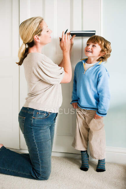 Madre midiendo a su hijo contra una puerta con un libro - foto de stock