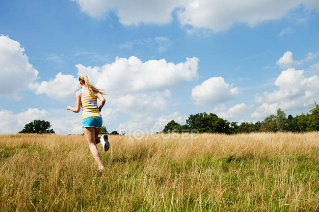 Mujer joven corriendo por un campo en un día soleado - foto de stock