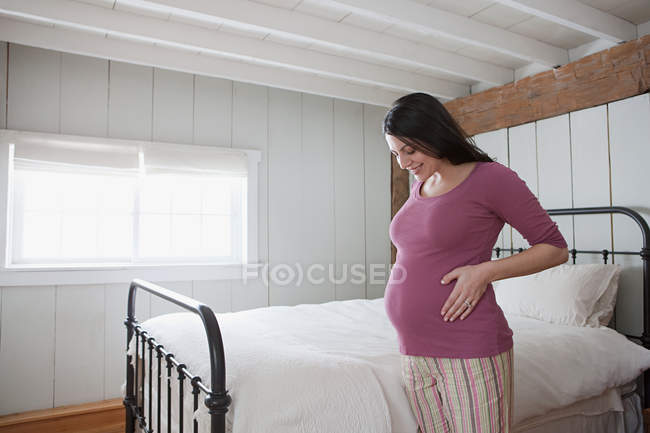 Mujer embarazada en el dormitorio sosteniendo el vientre - foto de stock