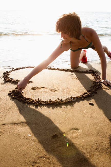 Woman drawing heart in sand on beach — Stock Photo