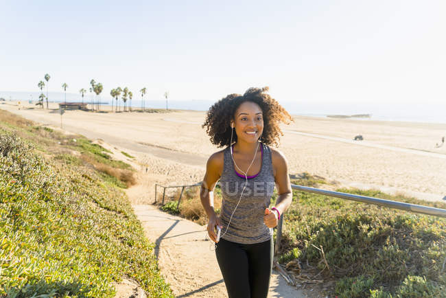 Mulher adulta média correndo ao longo do caminho pela praia — Fotografia de Stock