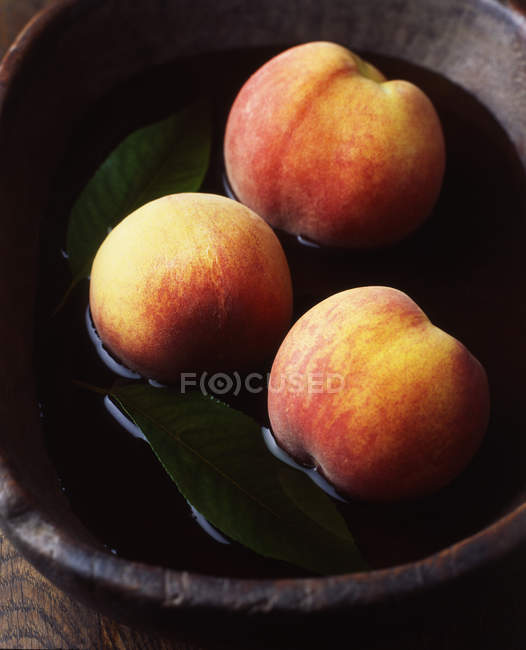 Peaches and leaves in rustic wooden bowl of water — Stock Photo