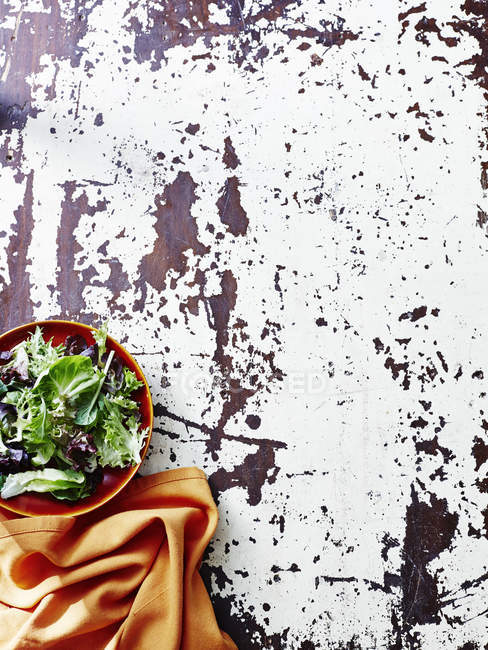 Натюрморт з листям салату в мисці та апельсиновою серветкою на сільському столі — стокове фото
