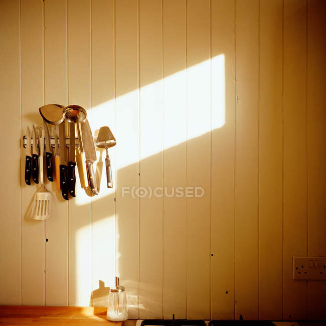 Utensilios de cocina colgados en la pared con luz solar - foto de stock