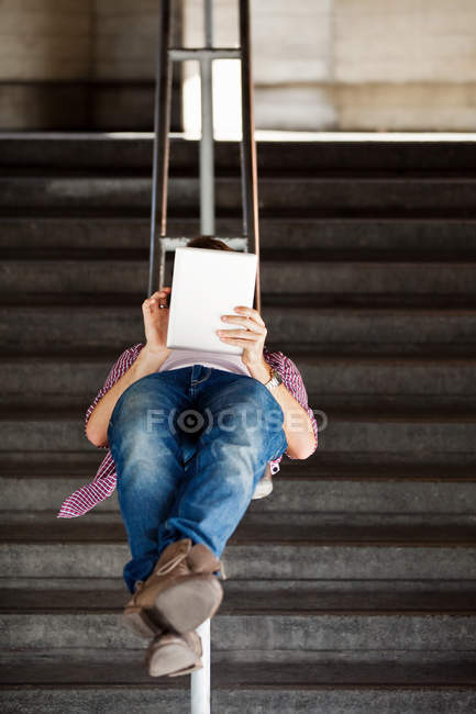 Un joven acostado boca arriba, usando una tableta digital - foto de stock