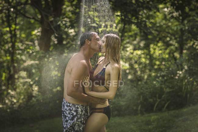 Mature man and young girlfriend kissing under garden shower — Stock Photo