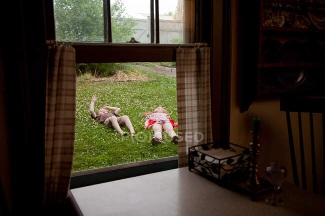 Вид через окно мальчика и девочки, лежащих в саду — стоковое фото