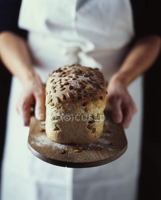 Жіночий пекар, що тримає свіжий запечений хліб на дерев'яній дошці — стокове фото