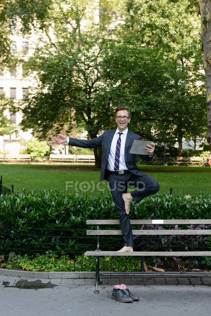 Businessman with digital tablet standing on one leg on bench — Stock Photo