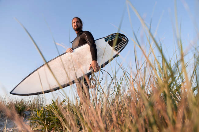Серфер, держащий доску для серфинга в траве — стоковое фото