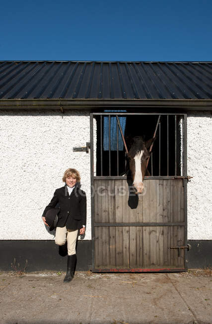 Niño de pie junto a establos de caballos - foto de stock