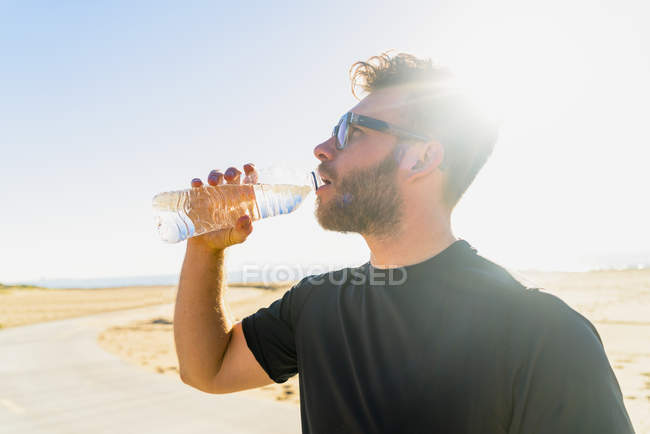 Молодий чоловік, на пляжі, п'є з пляшки води — стокове фото